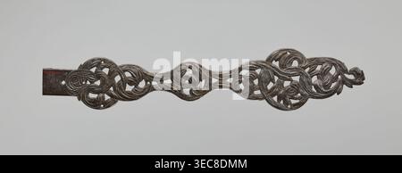 Hinge, openwork strap hinge from a pair: at one end a flat bar bent at a right angle and rolled into a sleeve, the remaining openwork part with a repoussé twig motif, chiseled and engraved; 2nd half of the 17th century; Central Europe; locksmithing., A long, narrow carved object with an openwork, intertwined flowing design resembling vines and leaves, predominantly dark brown with lighter brown highlights, set against a pale gray background; the carving includes a rectangular solid section at one end that is darker brown, and the overall piece has a slightly weathered, textured surface. Stock Photo