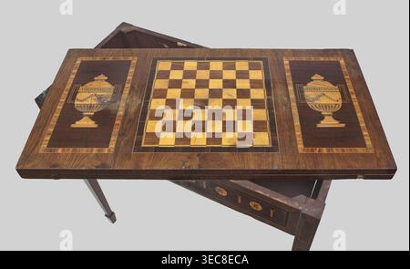Game table, games, classicism style, rosette ornament, chessboards, vases, classicist. Rectangular game table, square when unfolded, supported by four angular, converging legs with wedge feet; veneered and inlaid. The top is divided into three rectangular fields, enclosed by a ribbon and two veins, filled with vases outermost and a chessboard. 18th/19th century, Central Europe, possibly Gdańsk. Furniture; game furniture. Height 77 cm, width 42.5 cm, depth 86 cm., A wooden tabletop with a decorative inlaid chessboard at its center and a decorative panel on each side, all in tones of brown, tan, Stock Photo