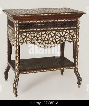 Side table, Rectangular side table with drop-down desks on each side and a bottom shelf, inlaid with mother-of-pearl and bone in geometric and plant patterns. Straight, angular legs that are S-shaped at the bottom and topped with brass rollers. Wide openwork frame filled with a dense lattice of turned elements mashrabiya. Tabletop, desks, frame, and shelf edge decorated with geometric braid forming rosettes; shelf covered with stars with hexagonal fields forming a network. Desk supports imitate bamboo. 19th century, 2nd half; Syria . Furniture, table. Dimensions: height 82 cm, width 100 cm, Stock Photo
