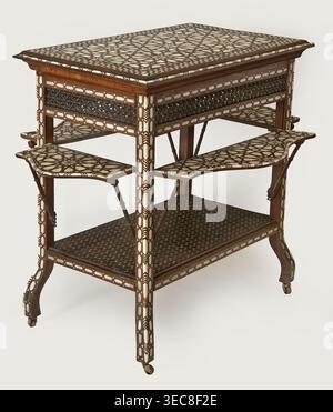 Side table. Rectangular side table with drop-down desks on each side and a bottom shelf, inlaid with mother-of-pearl and bone in geometric and plant patterns. Straight, angular legs S-shaped at the bottom, topped with brass rollers. Wide, openwork frame filled with a dense lattice of turned elements mashrabiya. Tabletop, desks, frame, and shelf edge decorated with geometric braid forming rosettes on the surfaces. Shelf covered with stars with hexagonal fields in the center, forming a network. Desk supports imitate bamboo. 2nd half of the 19th century. Syria, furniture, table. Dimensions: Stock Photo