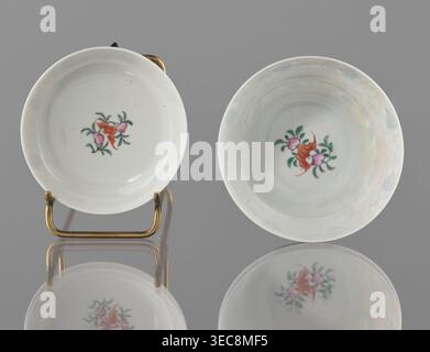 Bowl with lid; Chinese colored porcelain; Qing dynasty (Qianlong period, 1736–1795), Qing style; decoration: bats, longevity shou character, lotus tendrils, lotuses, peaches; vessel height 9 cm, diameter 10.7 cm; maker: Ignacy Jan Paderewski (1860–1941) mentioned (inscription/association)., A pair of shallow round dishes with a glossy white surface sit side by side on a reflective gray surface; each dish has a small central floral motif in pink, green, and orange, and one dish is propped on a small brass stand showing its brass color and curved shape, while the other rests directly on the Stock Photo