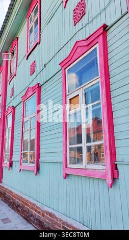 Colorful wooden house facade with bright pink decorative window frames on pastel blue walls. The vibrant architectural scene reflects traditional Stock Photo