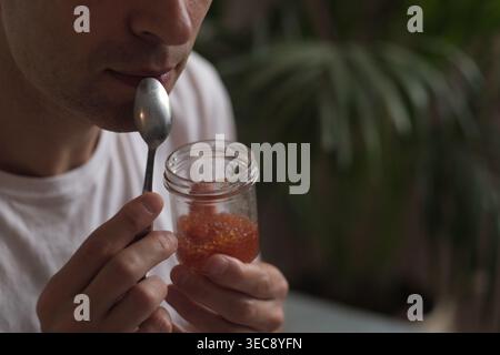 Man with a glass jar of salmon caviar pauses before tasting, in calm daylight. The photo connects to luxury minimalism, mindfulness, and authentic Stock Photo
