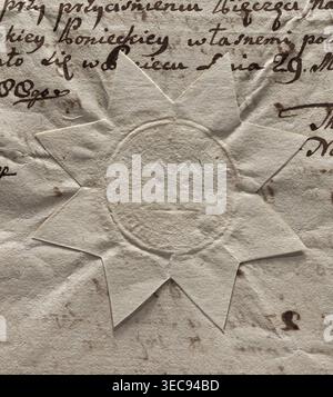 Round seal of the town of Poniec. In the field of the seal, two towers covered with conical roofs. One window in each tower. Between the towers, at the height of the roofs, a star. Illegible inscription on the rim. 1788, Poland., A close-up of wrinkled, aged paper showing a star-shaped embossed seal made of the same pale beige paper, with a circular impression and faint raised patterns in its center; the paper surrounding the seal is creased and stained, with several brown ink marks and smudges and a few darker brown spots, and visible handwritten strokes in dark brown ink at the top and right Stock Photo