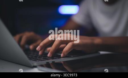 Man hands typing on laptop keyboard at night. Professional person working online, programming, or browsing internet in dark office. Concept of technol Stock Photo
