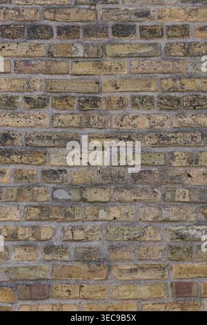 Weathered yellow and beige brick wall, with soot marks and visible mortar lines, showing aged texture and rough surface in vertical composition. Stock Photo