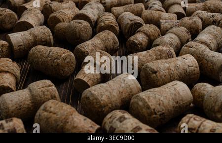 A high-angle, close-up shot of various natural wine and champagne cork stoppers scattered on a dark wood surface, emphasizing texture, sustainability, Stock Photo