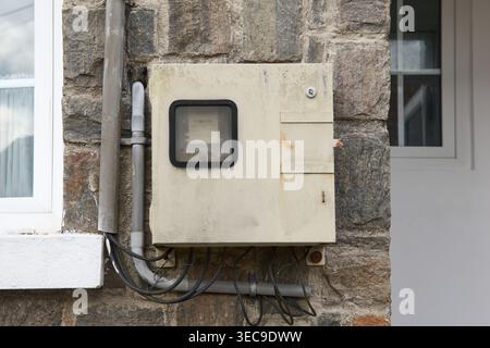 metal electrical utility box on grey stone wall, exposed wires and conduit pipes, soft focus home inspection and electrical service Stock Photo