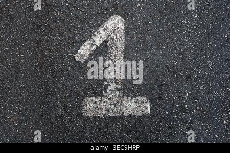 Close-up of a large, faded white painted number 1 stenciled on coarse dark gray asphalt, ground level view, weathered texture Stock Photo