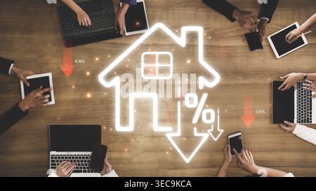 Hands Using Laptops and Tablets With Home Icon and Percent Symbols Signifying Real Estate Trends and Market Changes on Wooden Table Sigmoid Stock Photo