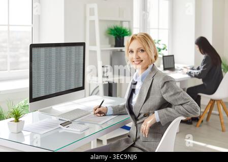 Confident businesswoman sitting at desk, working with financial data and analyzing spreadsheet. Stock Photo