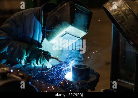 Industrial worker welding metal component with arc welding technique. Fabrication process with sparks, smoke, and protective gear in factory. Stock Photo