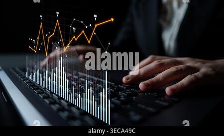A business professional is engaged in analyzing complex financial data trends on a laptop. The image features dynamic charts and graphs illuminating t Stock Photo
