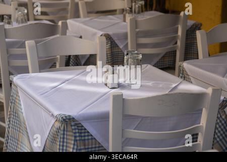 A close-up of a classic Greek tavern table, featuring blue-and-white checkered undercloths and crisp white top linens in Plaka, Athens. Stock Photo