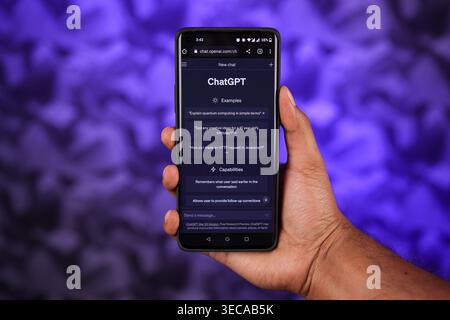 Chatgpt interface on Mobile holding by a hand with abstract blue background, this is an Artificial intelligence Ai app to ask Questions. Dark mode screen. Stock Photo