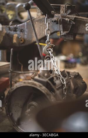 An old engine part is being lifted by a chain and hook in a workshop, showcasing the mechanics of repair Stock Photo