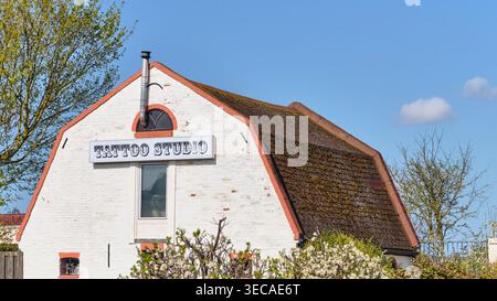 Tattoo Studio Sign On White Building In Spanbroek, Netherlands, With Blue Sky And Green Trees Stock Photo