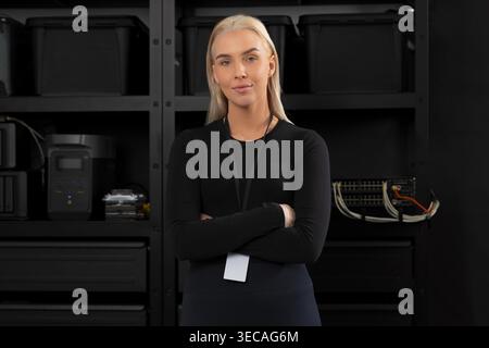 Confident Caucasian woman IT technician stands with arms crossed in a modern data center server room Stock Photo