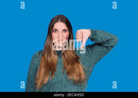 Young woman frowning and showing thumbs down against a blue background Stock Photo