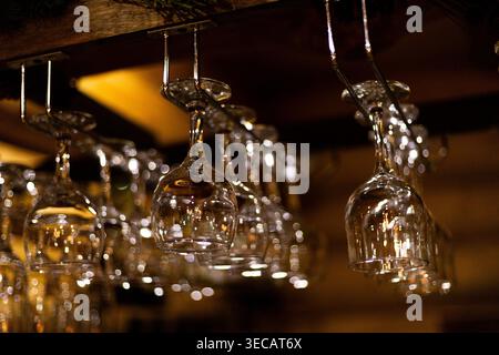 Clear glass wine glasses displayed upside down on a rack. Low light setting with warm, soft bokeh in the background. Focus on reflections and transpar Stock Photo