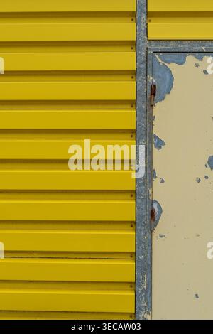 Close-up of a vivid yellow corrugated metal wall panel next to a weathered surface with peeling paint revealing layers of blue and cream, creating a s Stock Photo