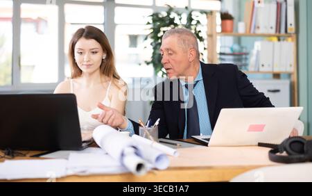 Mature man working in office, sitting at desk next to woman Stock Photo
