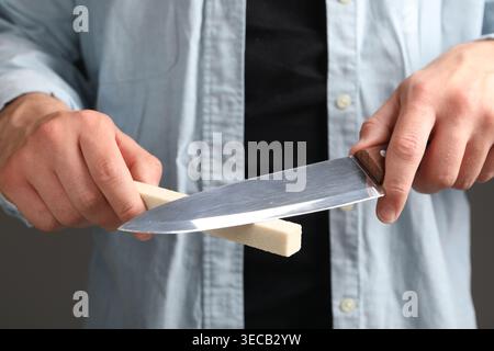 Man sharpening knife on grey background, closeup Stock Photo