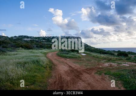Dirt Road Curving Through Coastal Landscape Under Cloudy Sky Stock Photo