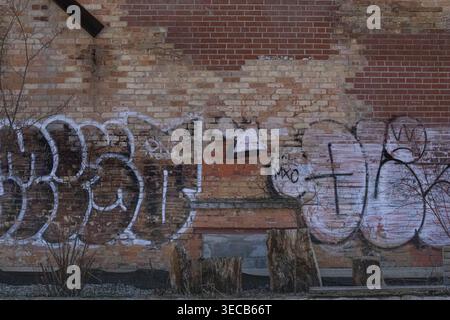Aged red brick wall with patchwork repairs and graffiti in white and black paint, showing worn urban texture and weathered surface. Stock Photo