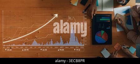 Aerial view of a collaborative workspace featuring hands analyzing graphs and charts on a table, representing business growth and strategic planning. Stock Photo