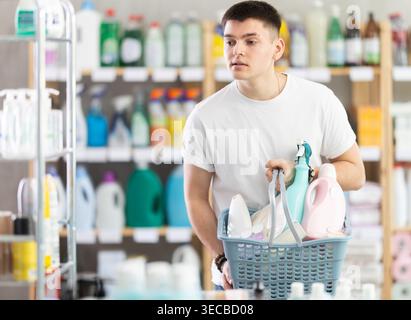 Guy selects various household cleaning products for cleaning the house with full basket of various purchases Stock Photo