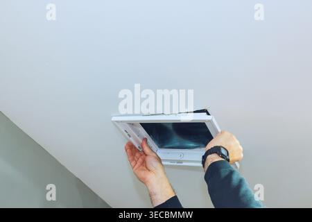 Contractor is taking off an access ceiling vent panel from ceiling while standing in room. Stock Photo