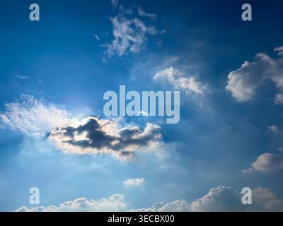 Blue sky with bright sunrays peeking from behind dark clouds, creating a dramatic and hopeful atmospheric scene. Stock Photo