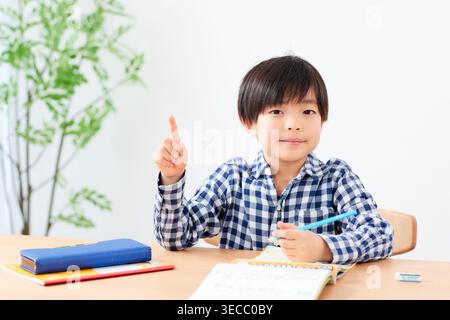 Japanese elementary school boy smiling pointing up with an idea studying Stock Photo