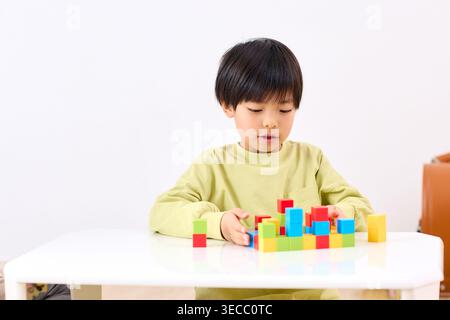 Japanese boy focused on building colorful blocks on a white table indoors Stock Photo