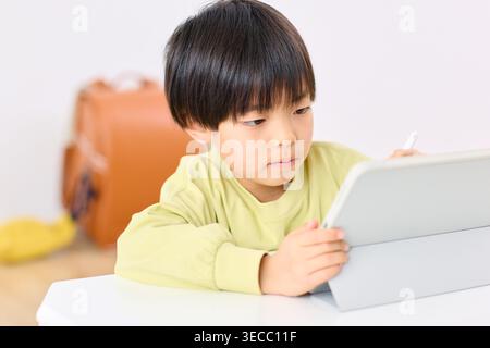 Japanese elementary school boy focused on tablet learning at home Stock Photo