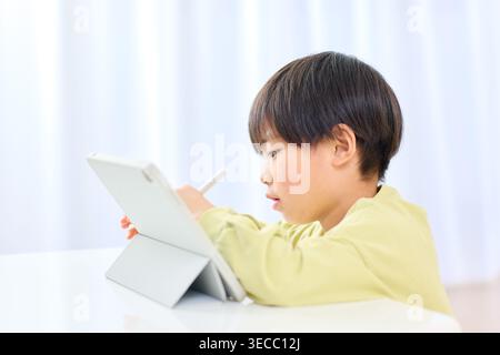 Focused Japanese boy learning with a tablet and stylus pen at home Stock Photo