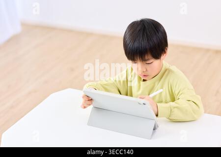 Japanese elementary school boy focused on tablet learning at home Stock Photo