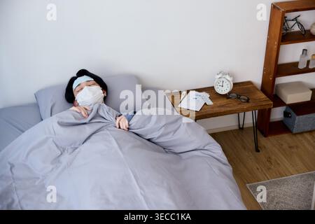 Sick Japanese young man resting in bed wearing a mask and cooling sheet Stock Photo