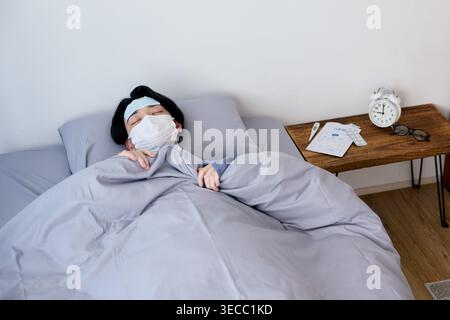 Sick Japanese young man resting in bed with mask and cooling sheet Stock Photo