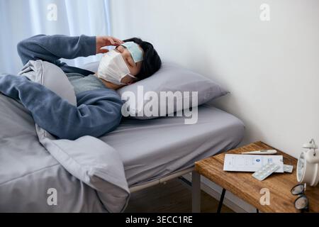 Sick young Japanese man resting in bed at home with mask and cooling sheet Stock Photo