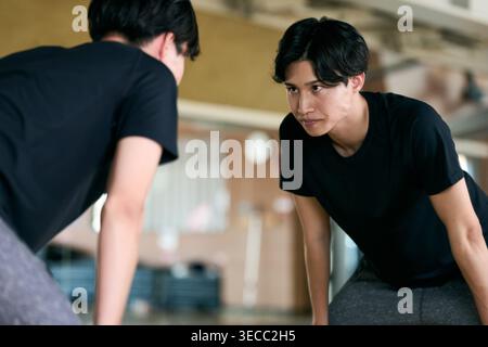 Japanese young man bending forward checking form in mirror at gym Stock Photo