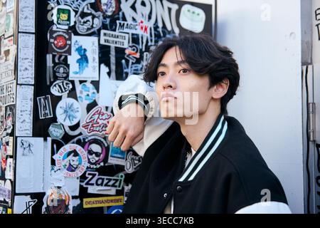 Thoughtful Japanese young man leaning against a graffiti wall Stock Photo