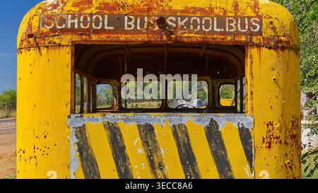 A rusting yellow and black striped skool bus with no windows sits abandoned on the side of the road in the sun in South Africa Stock Photo