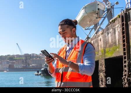 Asian cargo port worker using smartphone for logistics management Stock Photo