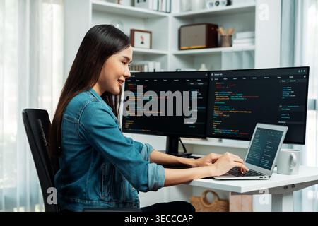 Smiling young Asian in IT developer creating with typing online information on laptop with coding program data of application, wearing jeans shirt. su Stock Photo