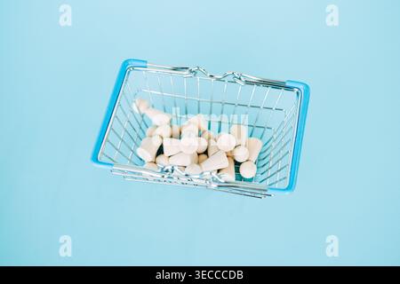 Wooden peg dolls lie inside miniature wire shopping basket against blue background. Talent acquisition strategy, recruitment process outsourcing Stock Photo