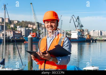 Asian worker wearing hard hat smiling at cargo port Stock Photo