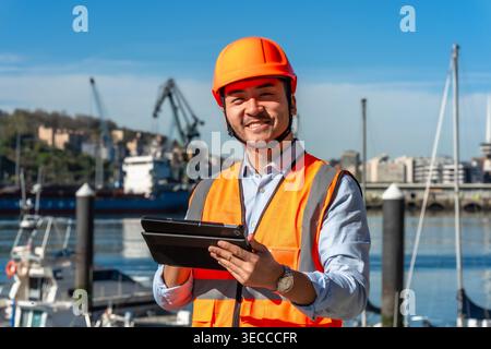 Asian worker wearing safety helmet holding tablet at port Stock Photo