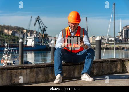 Port worker wearing safety vest checking tablet at harbor Stock Photo